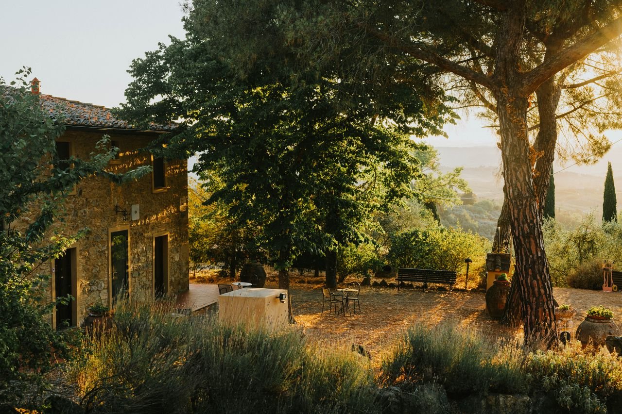 Idyllic countryside scene of Tuscany with rustic house and lush trees bathed in warm sunset light.